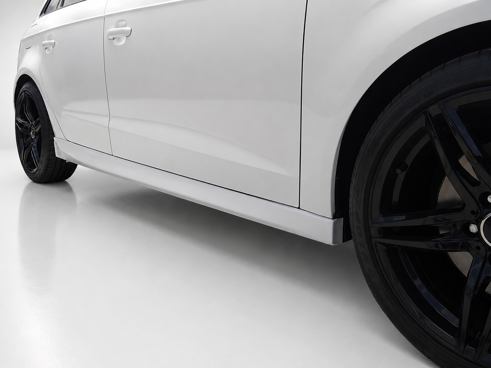 K152-003_2jpg - OPSHOLDERS Side view of a white car showing the doors, lower body panel, and a black alloy wheel with a glossy rim.