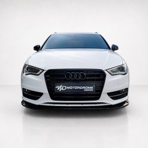 Front view of a white Audi sedan facing the camera in a studio setting, featuring a black grille and prominent four-ring emblem, with a Motordrome Design license plate-style badge on the bumper.