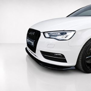 Front-right view of a white Audi car in a showroom, featuring a black grille and prominent headlight.