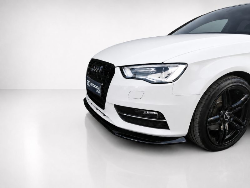 Front-right view of a white Audi car in a showroom, featuring a black grille and prominent headlight.
