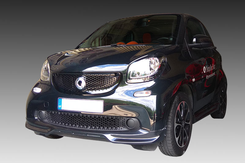 K154-001_1jpg - OPSHOLDERS Front three-quarter view of a dark, glossy compact car with a honeycomb grille and red side decals.