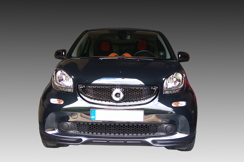 K154-001_2jpg - OPSHOLDERS Front view of a dark compact car facing the camera, with a chrome grille and orange seats visible through the windshield.