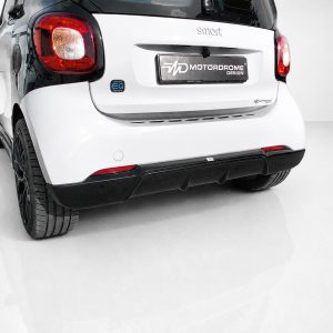 Rear view of a white Smart car on a glossy white floor, featuring red taillights and a MOTORDROME DESIGN license plate area on the hatch.