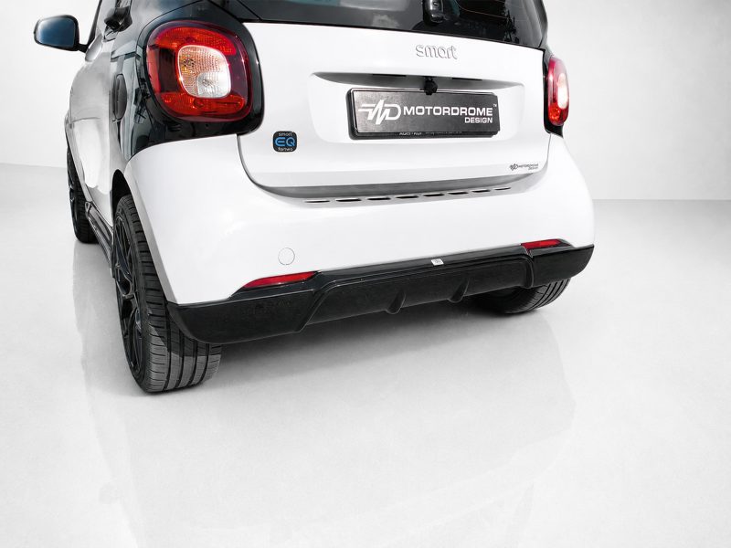 Rear view of a white Smart car on a glossy white floor, featuring red taillights and a MOTORDROME DESIGN license plate area on the hatch.
