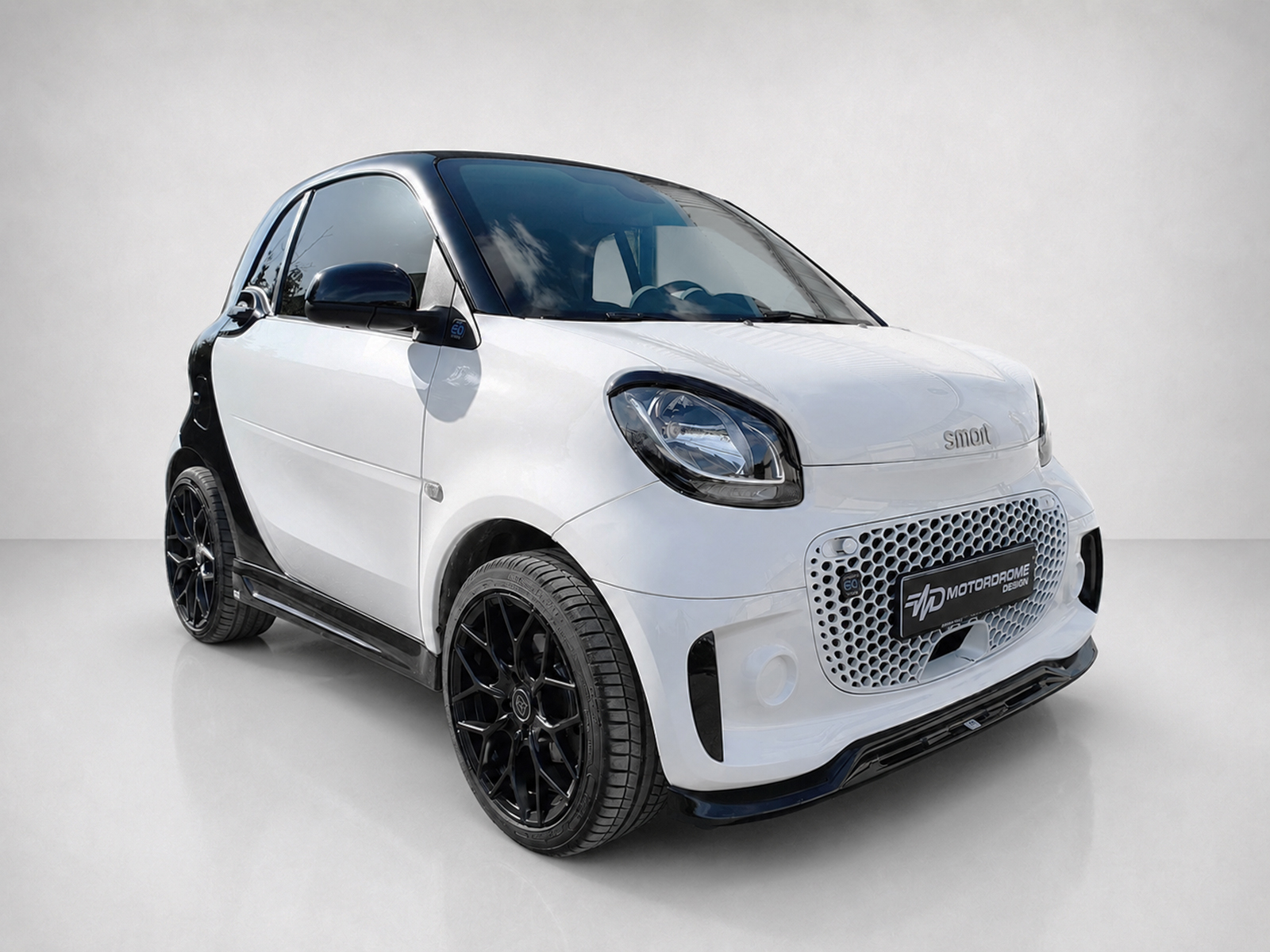 K154-003_1jpg - OPSHOLDERS White compact car with black roof and dark alloy wheels, shown in a studio setting (three-quarter front).