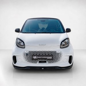 Front view of a white compact car facing the camera, featuring a honeycomb grille and glossy black accents on the sides and roof edge.