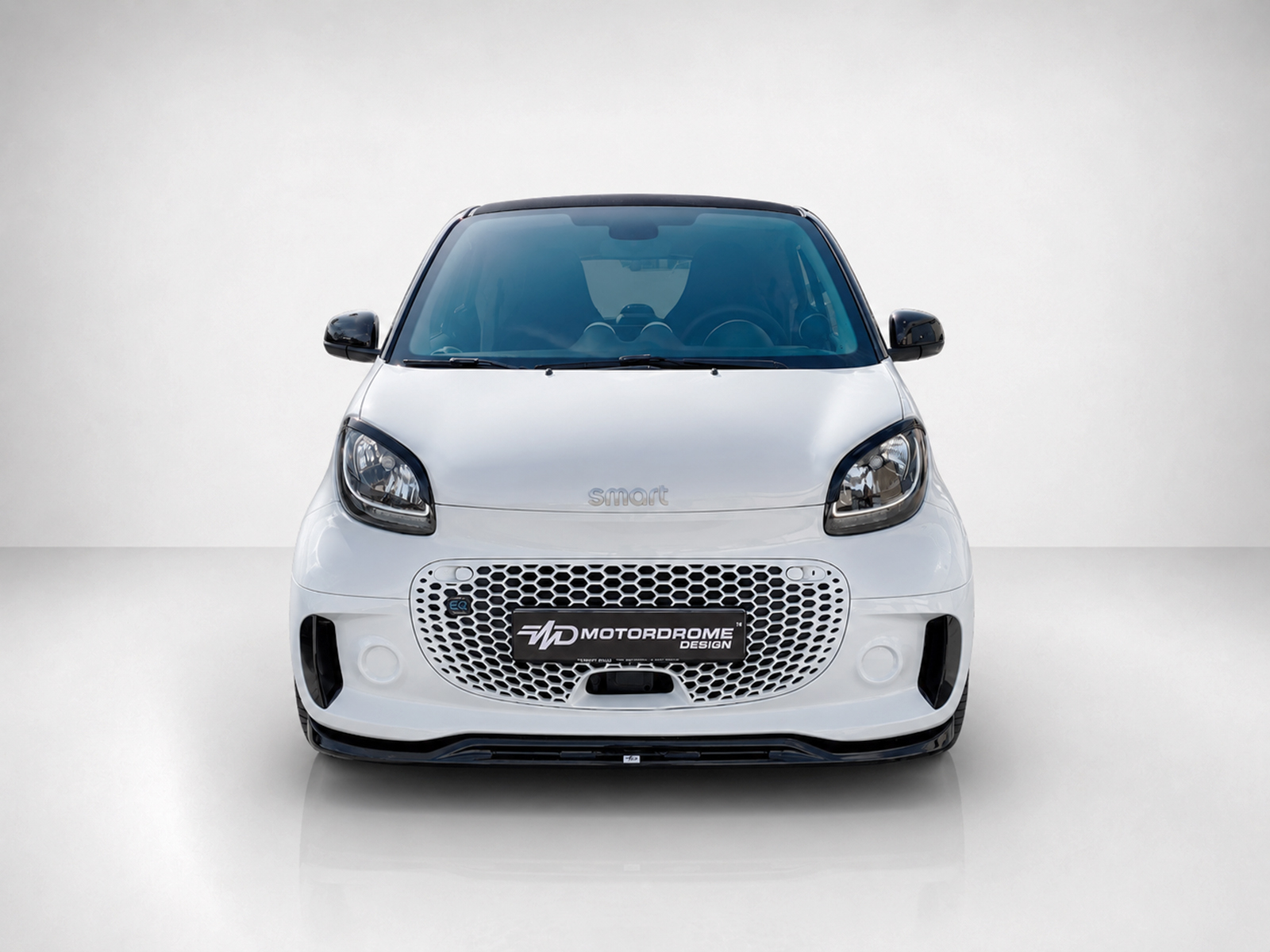 K154-004_1jpg - OPSHOLDERS Front view of a white compact car facing the camera, featuring a honeycomb grille and glossy black accents on the sides and roof edge.