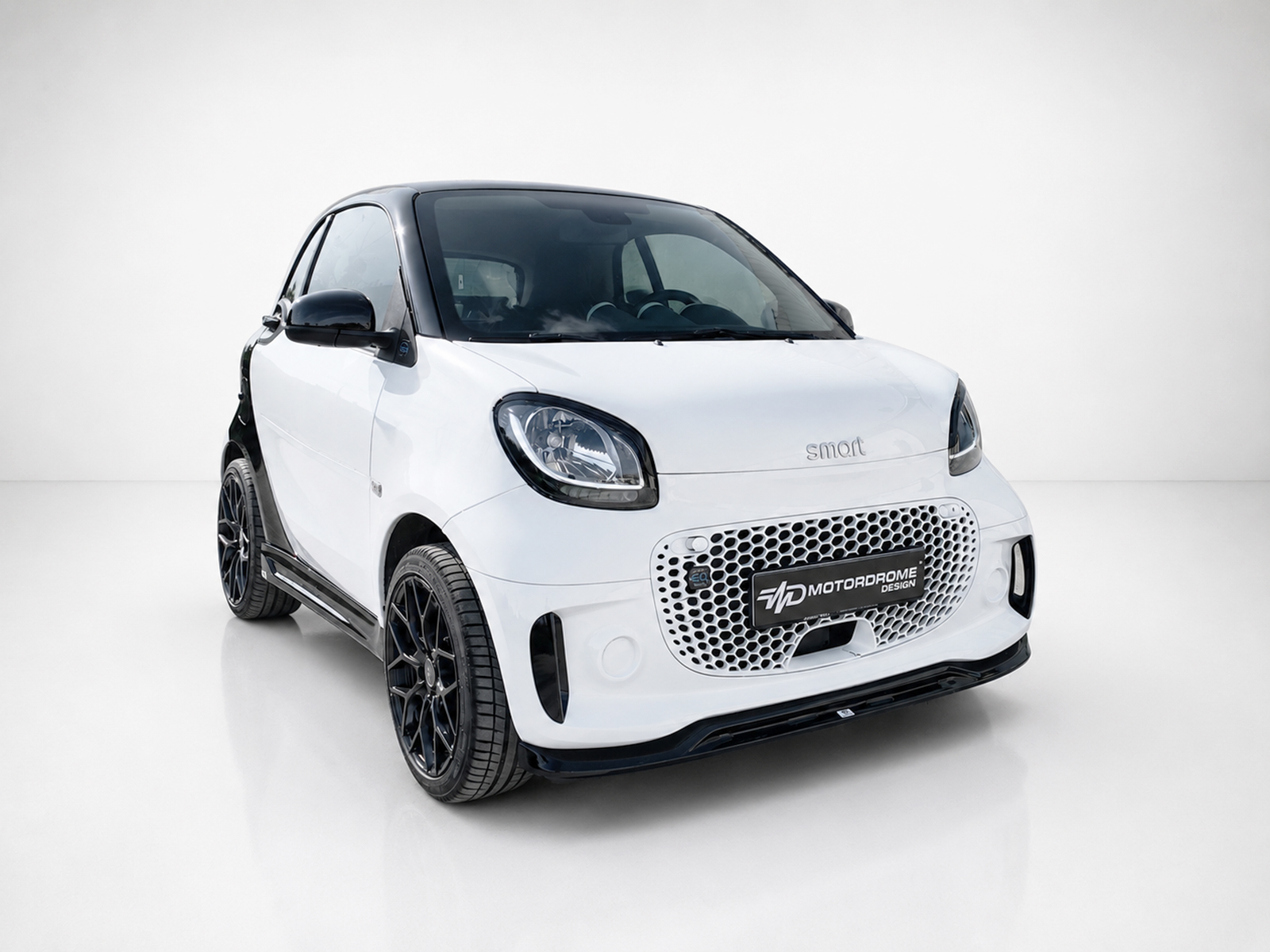 K154-004_2jpg - OPSHOLDERS White Smart car with black roof and honeycomb grille, angled front view in studio setting, front-left perspective, high polish.