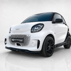 K154-004_3jpg - OPSHOLDERS White compact Smart car with black roof and prominent honeycomb front grille, set on a glossy studio floor with a Motorodrome Design plate.