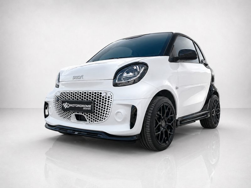 K154-004_3jpg - OPSHOLDERS White compact Smart car with black roof and prominent honeycomb front grille, set on a glossy studio floor with a Motorodrome Design plate.