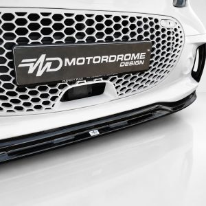 K154-004_5jpg - OPSHOLDERS Front end of a white car with a hexagonal honeycomb grille and a Motordrome Design license plate showing the brand name Motordrome Design (logo area visible).