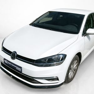 Front three-quarter view of a white Volkswagen sedan in a clean studio setting, showing the grille with the VW logo and sleek headlights.