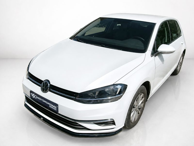 Front three-quarter view of a white Volkswagen sedan in a clean studio setting, showing the grille with the VW logo and sleek headlights.