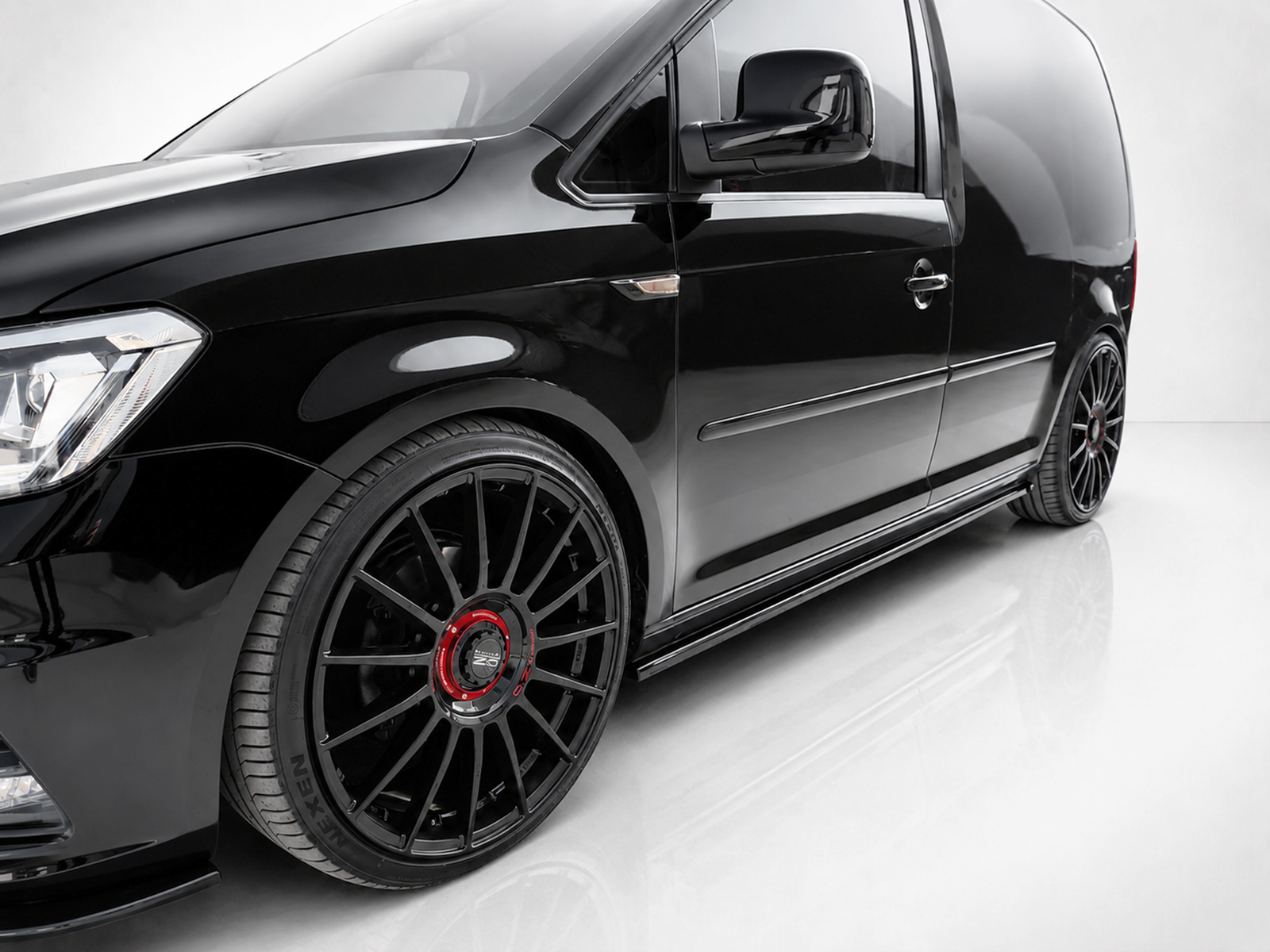 K157-003_2jpg - OPSHOLDERS Close-up of a glossy black van showing the front fender, door, and a large multi-spoke wheel with a red center cap.