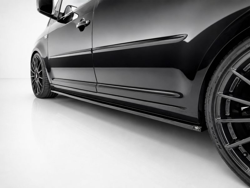 K157-003_3jpg - OPSHOLDERS Close-up of a glossy black car's side, showing the front wheel, door, and side skirt with alloy rims in sharp detail.
