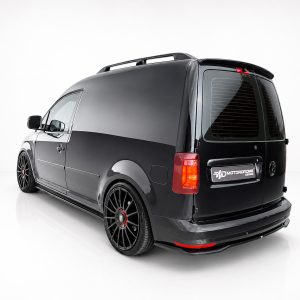K157-003_4jpg - OPSHOLDERS Rear three-quarter view of a glossy black van with large black aftermarket wheels in a white studio setting, showing its lowered stance and roof rails.