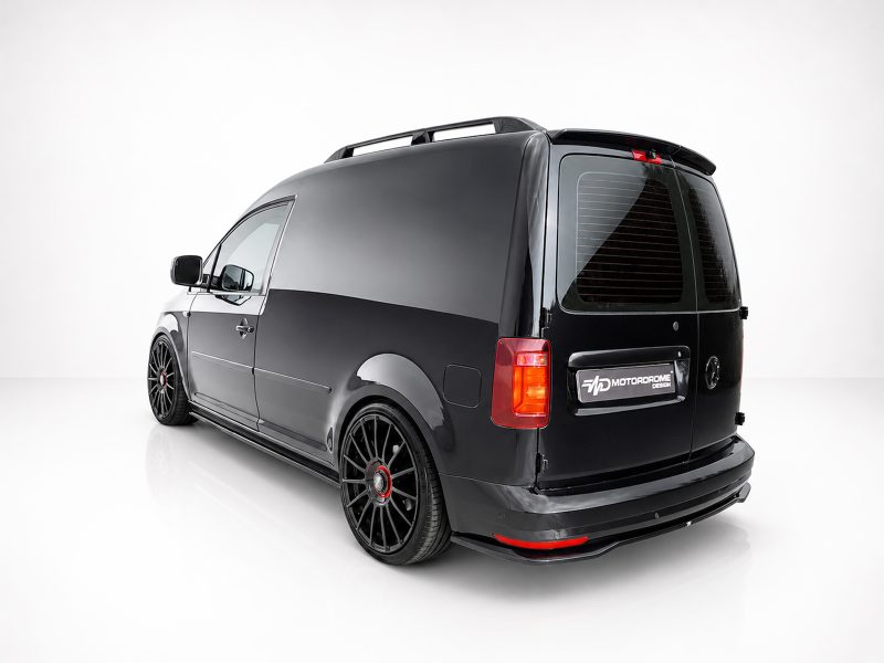 K157-003_4jpg - OPSHOLDERS Rear three-quarter view of a glossy black van with large black aftermarket wheels in a white studio setting, showing its lowered stance and roof rails.