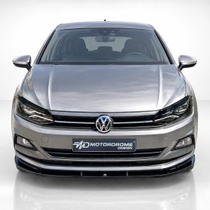 Front view of a silver VW car facing the camera, showing the grille, logo, and headlights in a studio setting with a dealership plate reading 'Motordrome Design'
