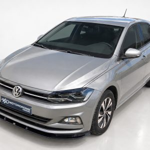 K162-001_2jpg - OPSHOLDERS Front-left angled view of a silver Volkswagen sedan in a bright studio showroom, glossy finish visible.