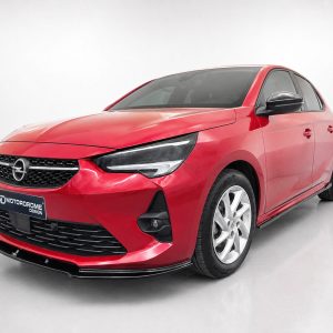 Red compact sedan shown in a three-quarter front view, featuring a black grille with an Opel emblem and sharp headlights, in a showroom.