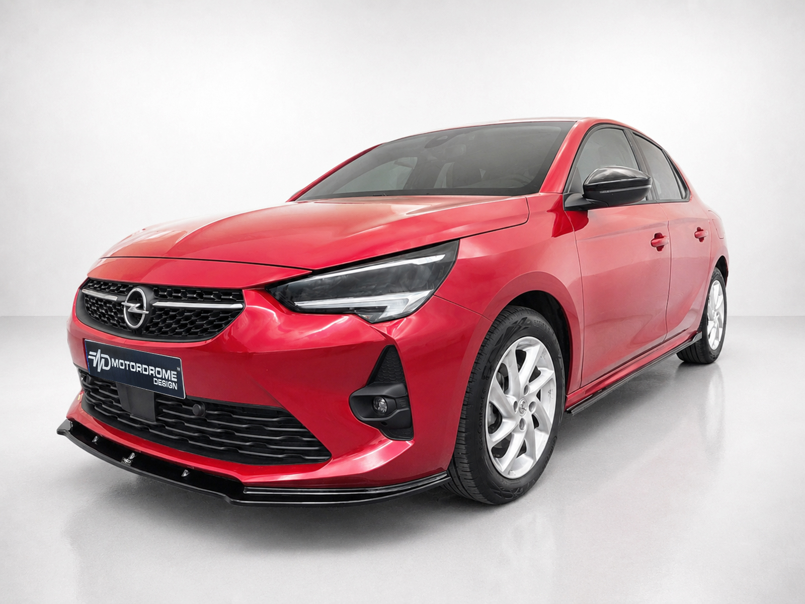 K163-001_1jpg - OPSHOLDERS Red compact sedan shown in a three-quarter front view, featuring a black grille with an Opel emblem and sharp headlights, in a showroom.