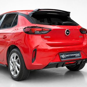 Rear view of a red Opel Corsa hatchback showing tail lights, rear badge, and spoiler in a studio setting with a black roof spoiler accessory visible on top of the tailgate.”,