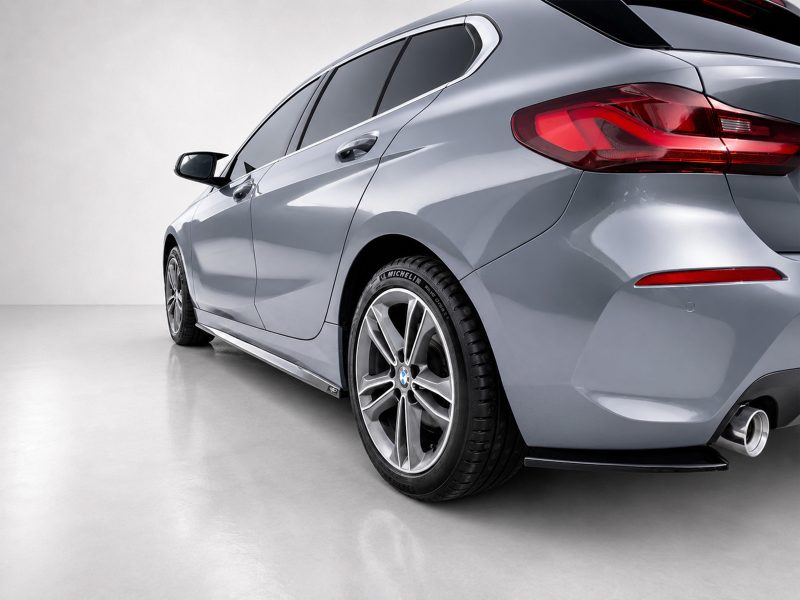 Rear three-quarter view of a silver BMW car in a studio, showcasing its alloy wheels and red taillights.