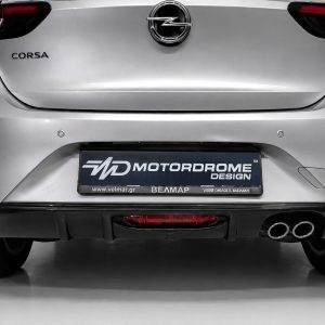 Rear of a silver Opel Corsa with emblem, Corsa badge, red taillights, and a MOTORDROME DESIGN plate in a showroom setting, showing dual exhausts.