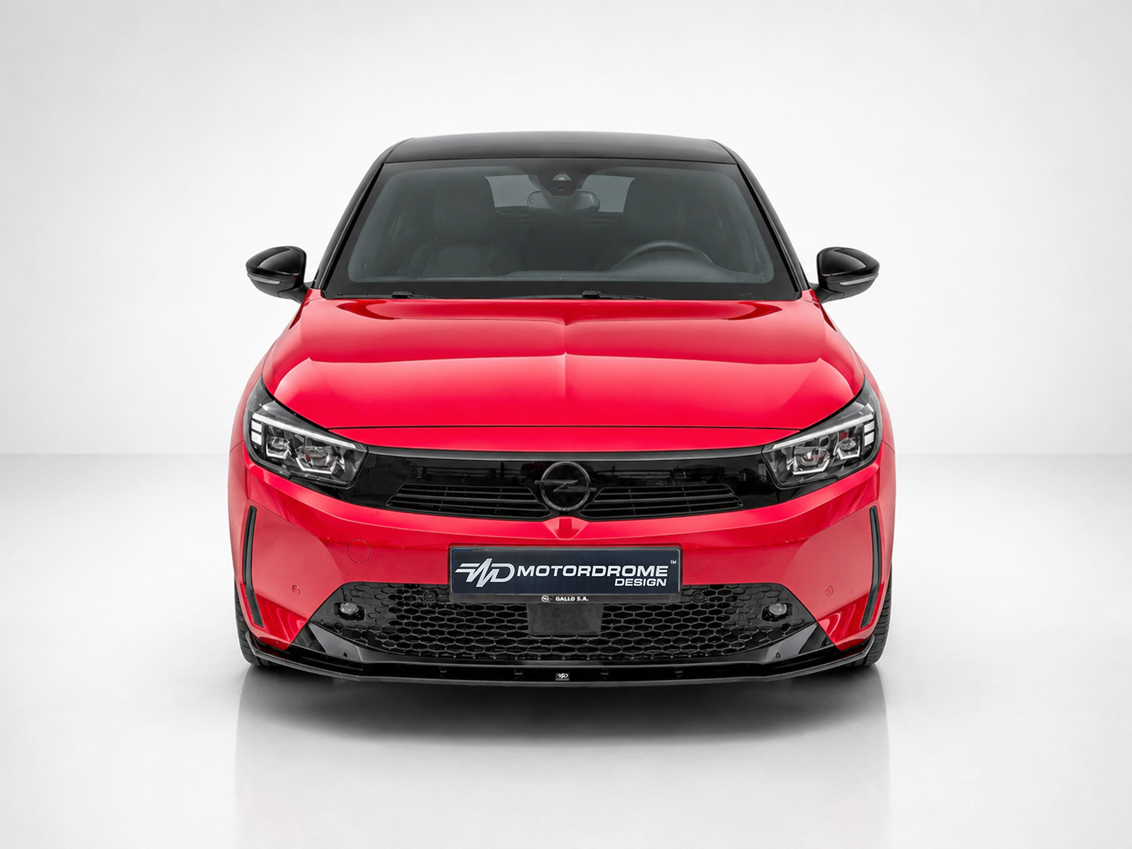 K163-006_1jpg - OPSHOLDERS Front-on view of a red car with a black grille, parked in a studio setting with a light gray background.