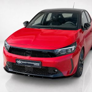 K163-006_4jpg - OPSHOLDERS Front three-quarter view of a red compact hatchback with a black roof and glossy black grille in a studio setting, showing Opel badge.