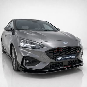 Gray Ford sedan shown from a front-left angle in a bright studio with a black honeycomb grille and LED headlights.