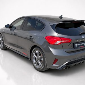 Rear three-quarter view of a gray Ford Focus hatchback with sporty wheels and a rear spoiler in a studio setting, showing dual exhausts on the right.