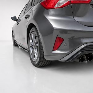 Rear three-quarter view of a gray sedan showing the tail lights, rear bumper, and quad exhaust pipes in a studio setting