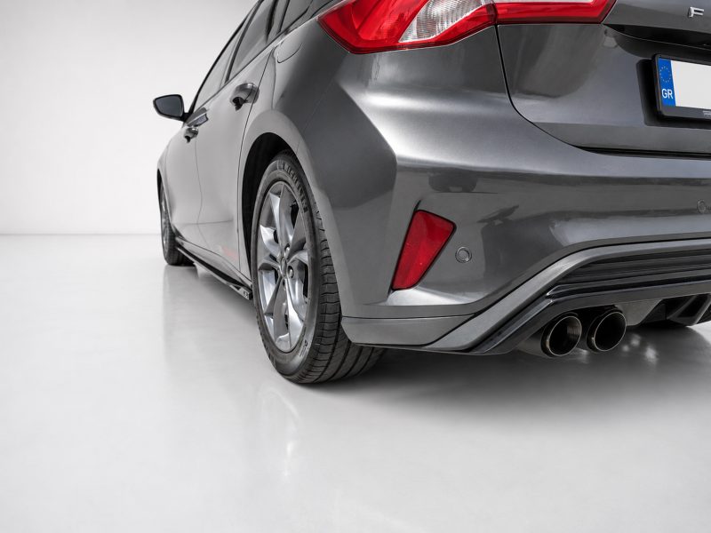 Rear three-quarter view of a gray sedan showing the tail lights, rear bumper, and quad exhaust pipes in a studio setting