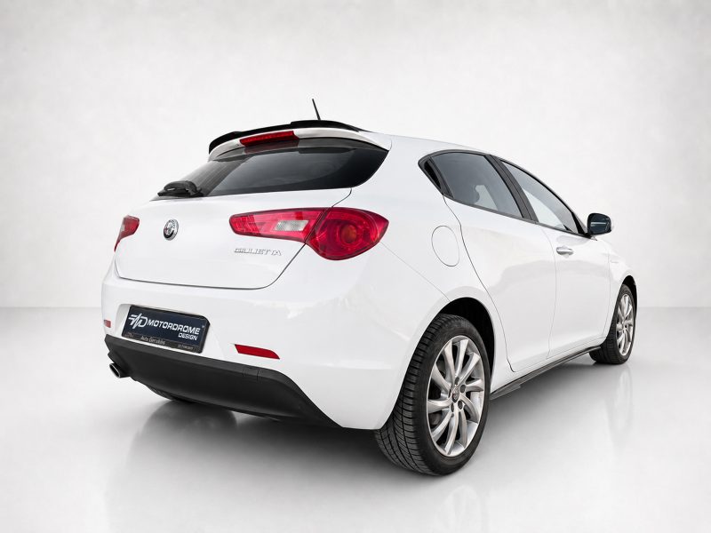 White Alfa Romeo Giulietta seen from the rear-right, parked in a studio backdrop.