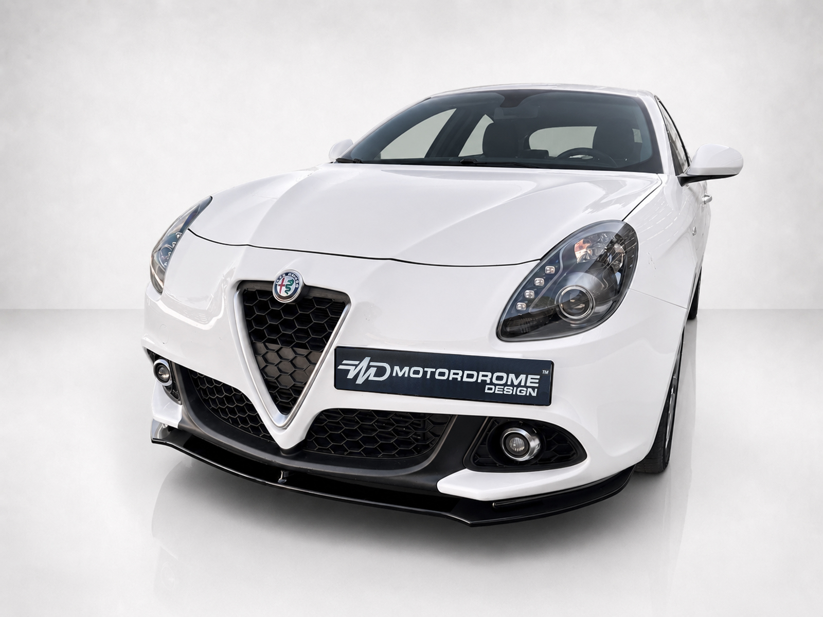K166-004_1jpg - OPSHOLDERS Front three-quarter view of a white Alfa Romeo sports car, showing the distinctive V-shaped grille and honeycomb lower grille with a MotorDrome Design plate.