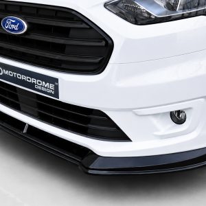 K167-001_2jpg - OPSHOLDERS Close-up of a white Ford car front, showing grille, headlight, and a MotorsDrome Design plate in the lower bumper area.