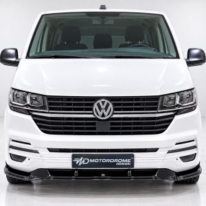 Front view of a white Volkswagen van showing the grille and headlights, showroom backdrop behind the vehicle, emblem centered on the grille.