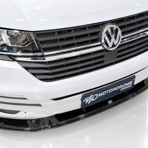 Front view of a white VW van showcasing the grille with the VW emblem and chrome accents, license plate reads 'Motorrome Design'