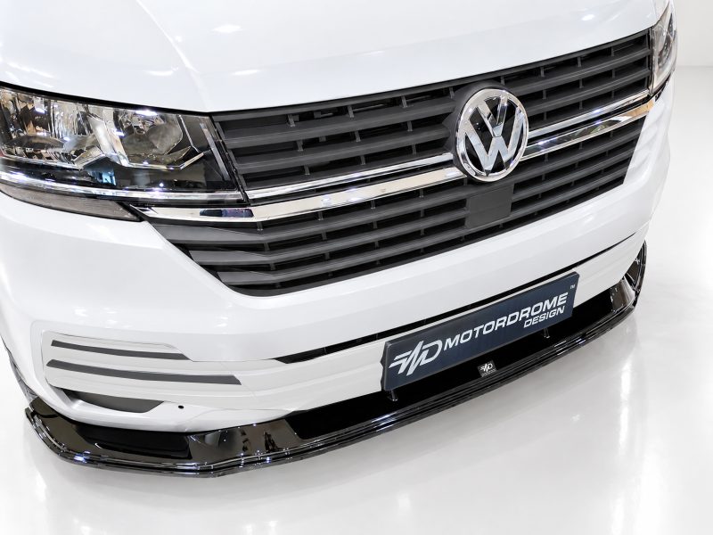 Front view of a white VW van showcasing the grille with the VW emblem and chrome accents, license plate reads 'Motorrome Design'