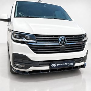 Front view of a white Volkswagen van with a chrome grille and prominent VW emblem, Motordrome Design plate on the bumper