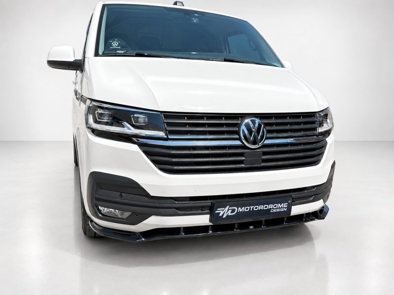 Front view of a white Volkswagen van with a chrome grille and prominent VW emblem, Motordrome Design plate on the bumper