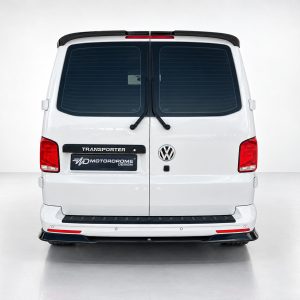 Rear view of a white VW Transporter van in a studio, showing rear doors, wiper blades, and a Motordrome Design plate on the bumper area.