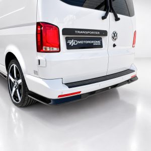 Rear view of a white VW Transporter van with a black 'TRANSPORTER' badge and a 'MD MOTORDROME DESIGN' plate on the tailgate.