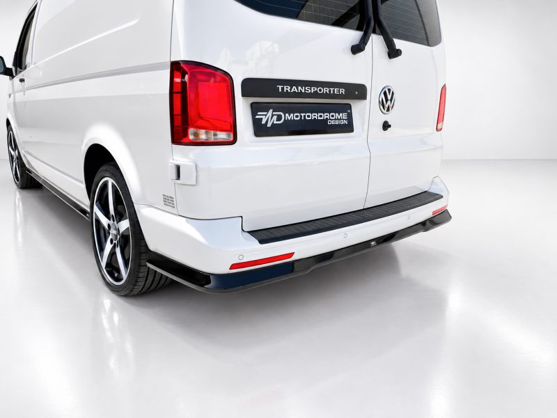 Rear view of a white VW Transporter van with a black 'TRANSPORTER' badge and a 'MD MOTORDROME DESIGN' plate on the tailgate.