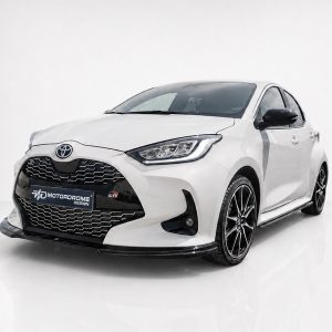 Front three-quarter view of a white Toyota sports sedan with a bold black grille and 'Motordrome Design' plate