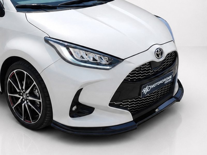 Front-left view of a white car showing the headlight, grille, and Toyota emblem on the hood.