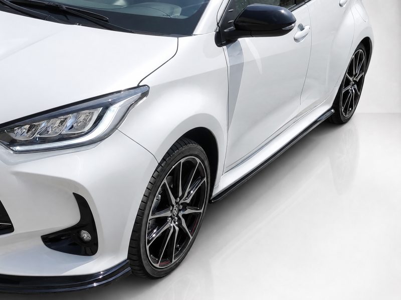 White modern car viewed from front-left, showing headlight, side mirror, and alloy wheel.