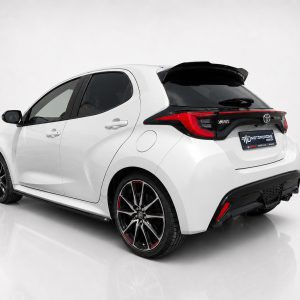 White Toyota Yaris hatchback, rear three-quarter view, with black rear spoiler and dark alloy wheels.
