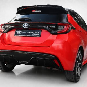 Rear view of a red Toyota Yaris Hybrid with a black spoiler and prominent taillights in a studio setting